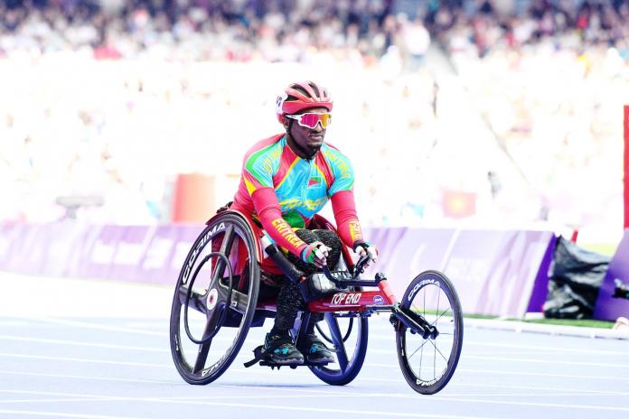 A wheelchair athlete in brightly coloured clothing and sunglasses on the Stade de France track